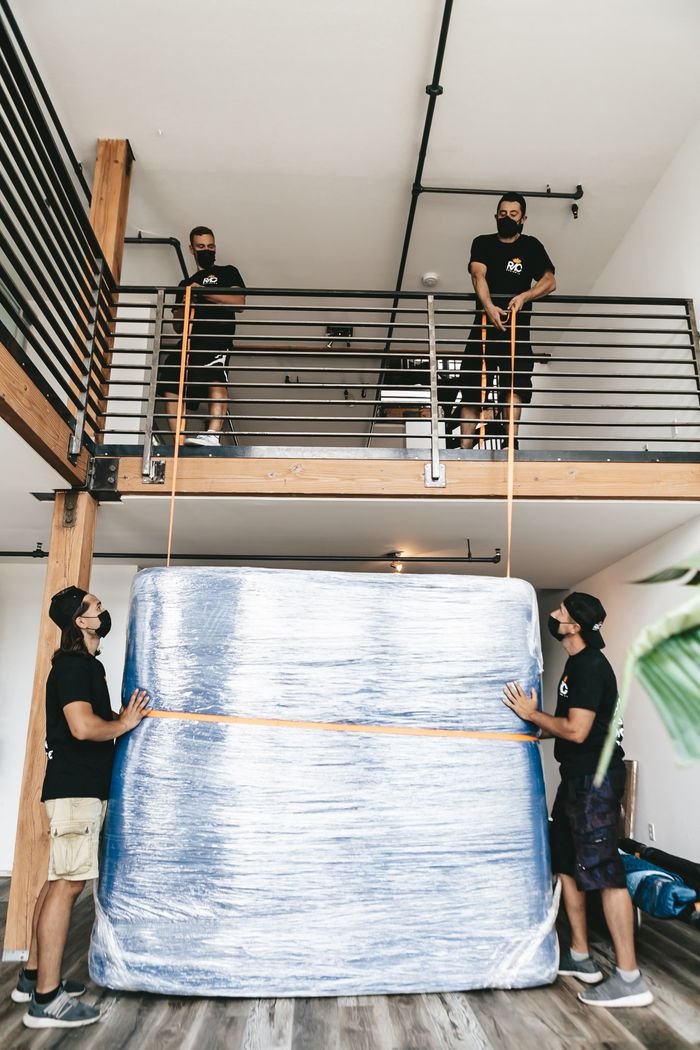 pexels photo 20706508 20706508 Four movers carefully lift a large wrapped object using straps indoors.