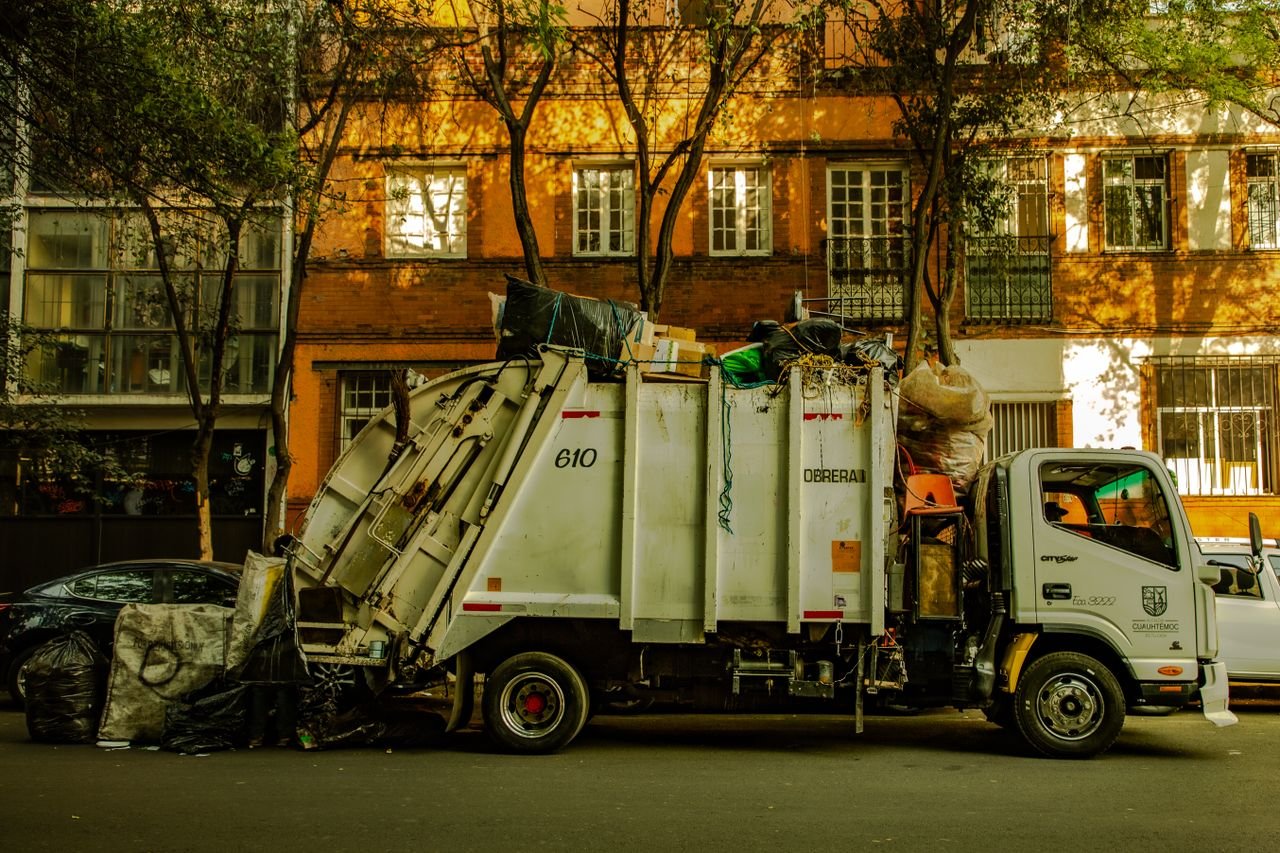 services-04 Garbage truck parked on an urban street in daylight, with residential buildings in the background.