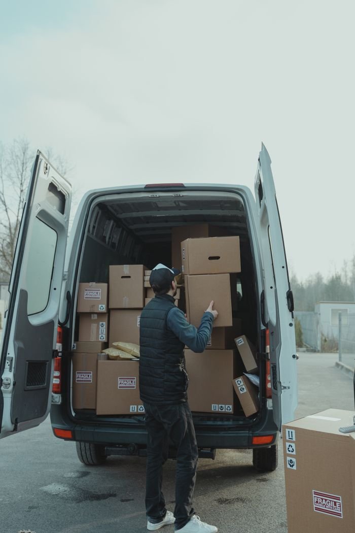 services-03 A delivery worker loading cardboard boxes into a van, preparing for shipment outdoors.
