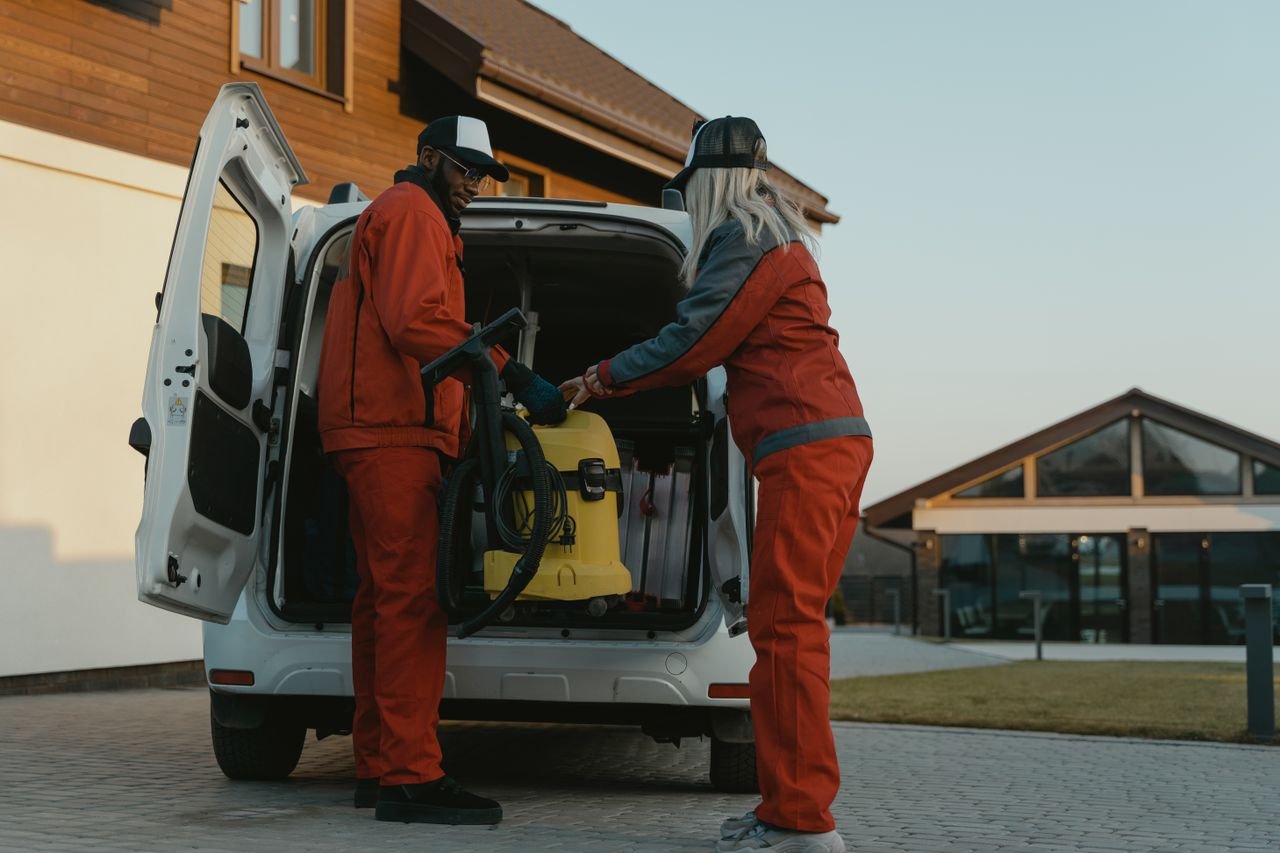 pexels photo 6195882 6195882 Two cleaners loading a vacuum into a van outside a modern building at dusk.